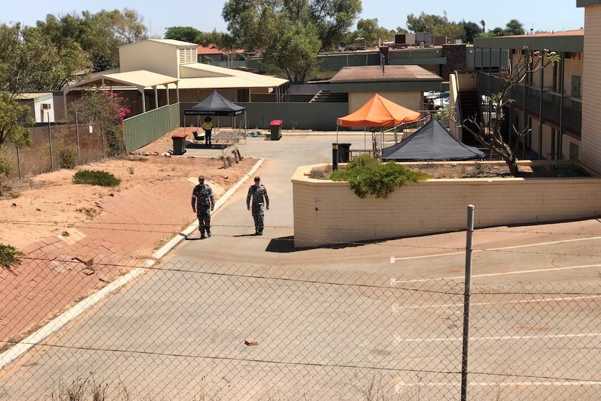 Two uniformed soldiers walk in an empty carpark at the back of a hotel with temporary tent shelters set up.