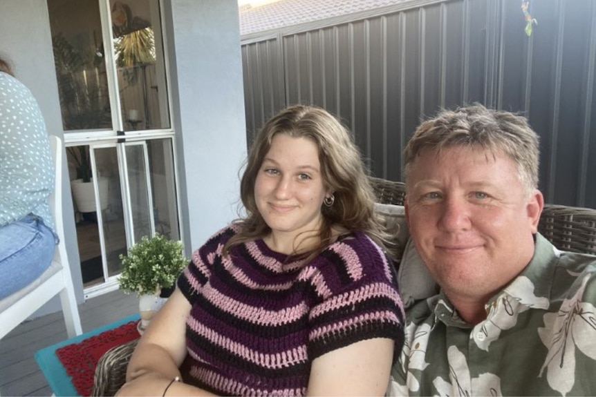 Young girl and her dad smiling at the camera, sitting on an outdoor lounge