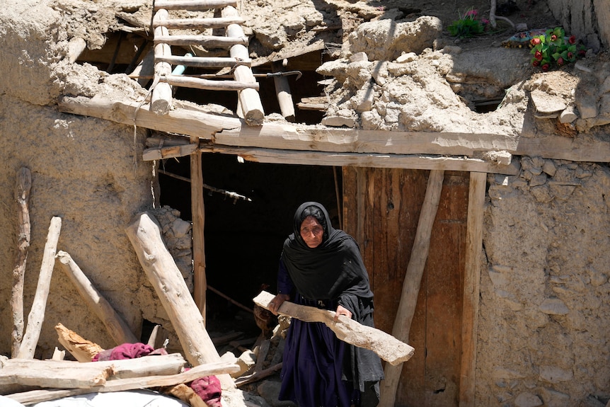 An Afghan woman carries a plank of wood next to her damaged home
