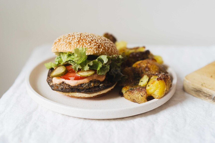 A mushroom burger on a plate with fresh lettuce and a side of smashed seaweed salt potatoes, a summer BBQ burger.