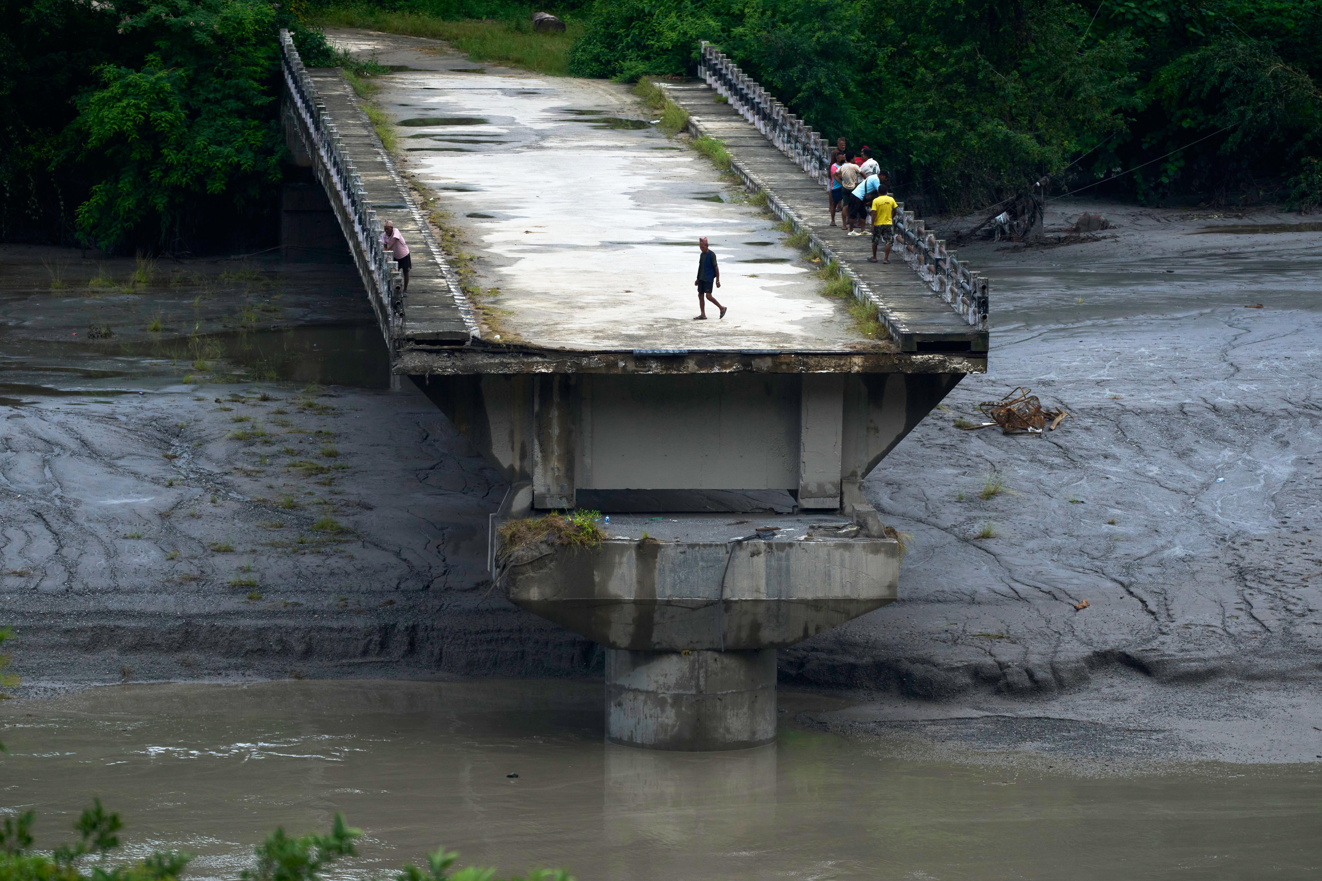 People stand on remnants of a bridge, the middle of which has been wiped away
