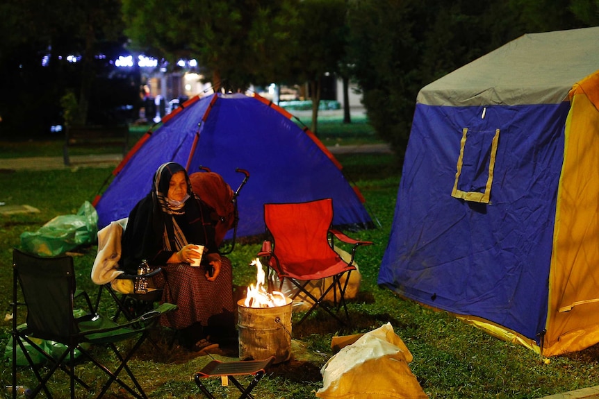 A local resident, staying outdoors for fear of aftershocks, tries to stay warm, in Izmir.