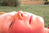 A pink faced boy lying in the sun on grass