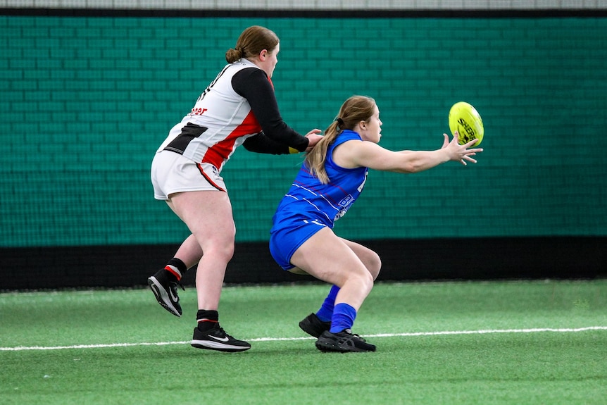 A woman reaches to catch a football on an indoor field.