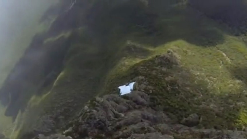 A base jumper in a white wing suit flies down Bluff Knoll in WA's Stirling Ranges