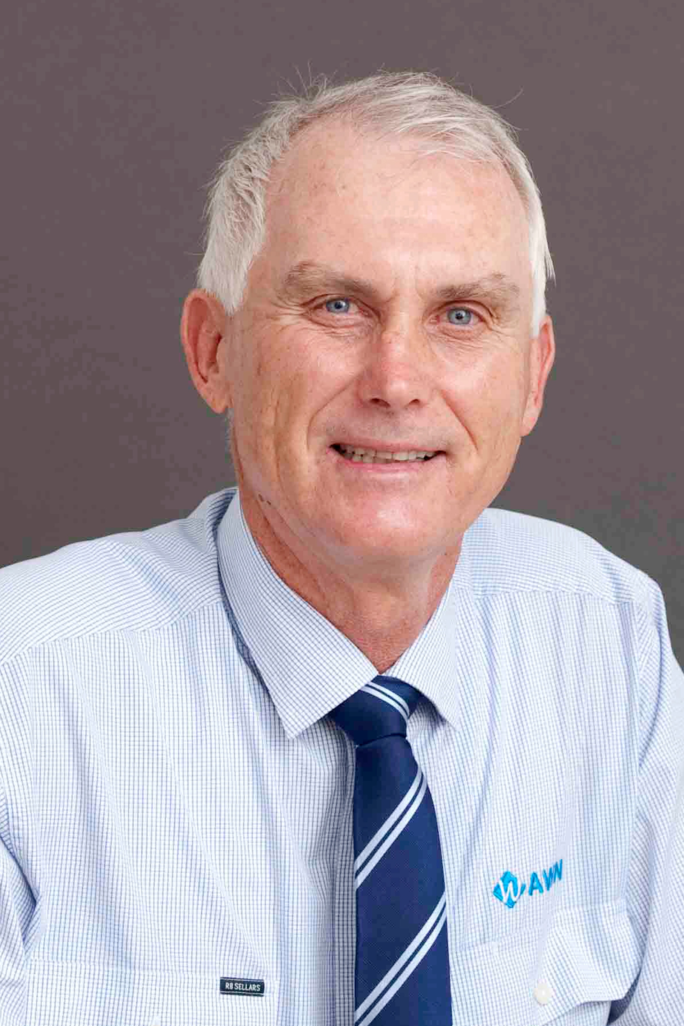 A man which white hair looks at the camera smiling, he is wearing a blue shirt.