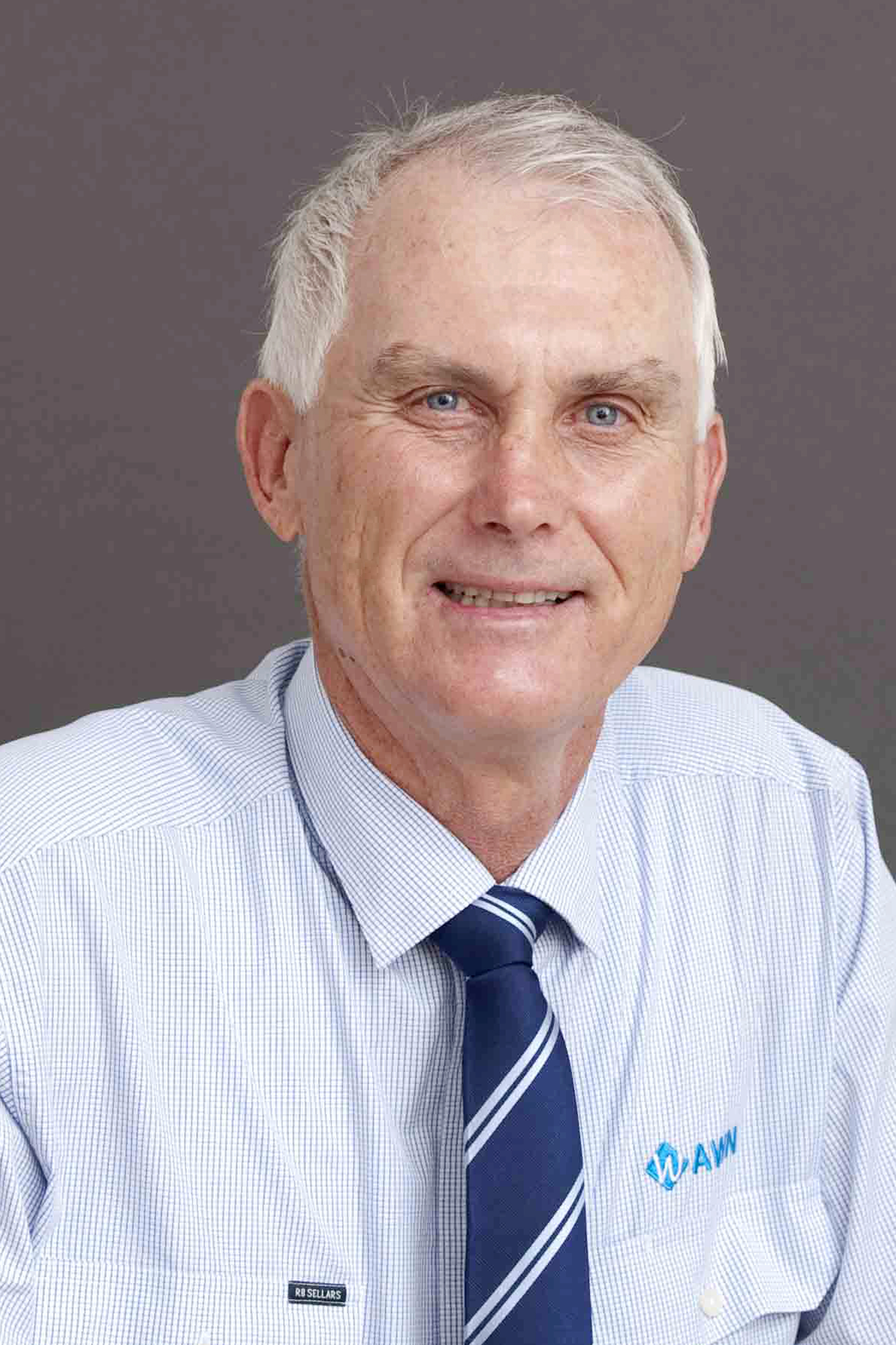 A man which white hair looks at the camera smiling, he is wearing a blue shirt.