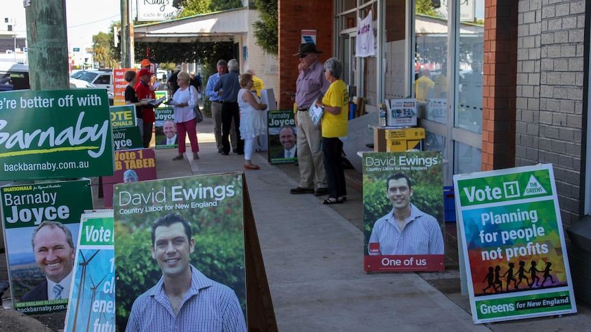 Candidate posters and people standing outside a building where people can pre poll for the New England by-election