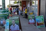 Candidate posters and people standing outside a building where people can pre poll for the New England by-election
