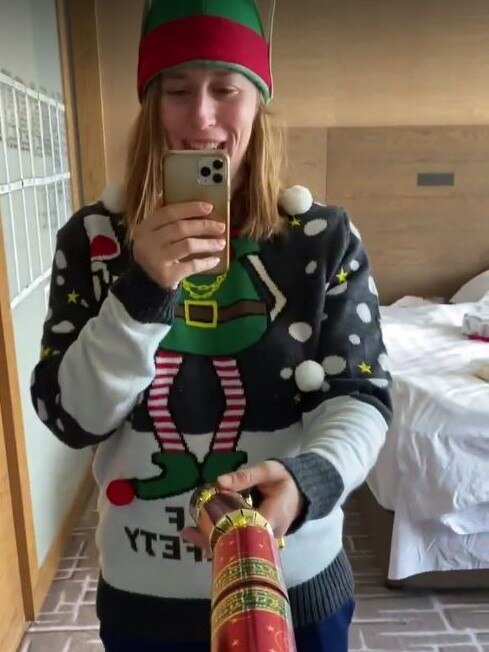 Alexandra Gummer wearing an elf hat and a Christmas jumper in a selfie and holding a bonbon in a mirror selfie.