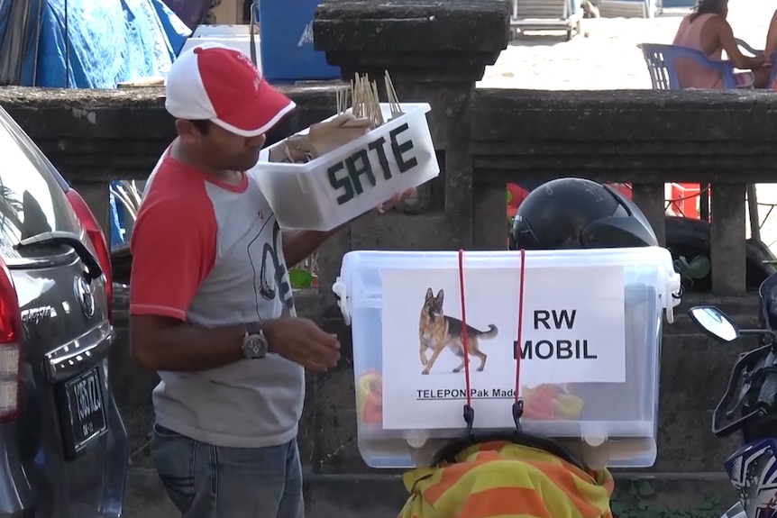 A dog meat vendor in Bali standing next to his moped