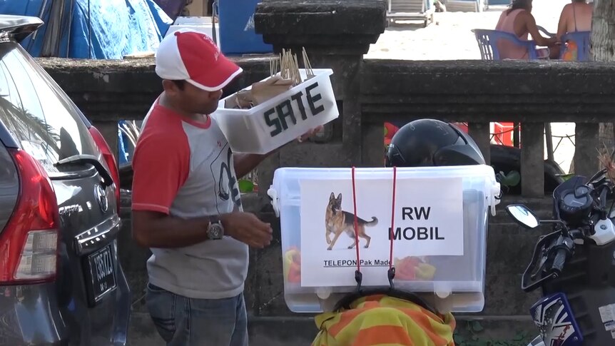 A dog meat vendor in Bali standing next to his moped
