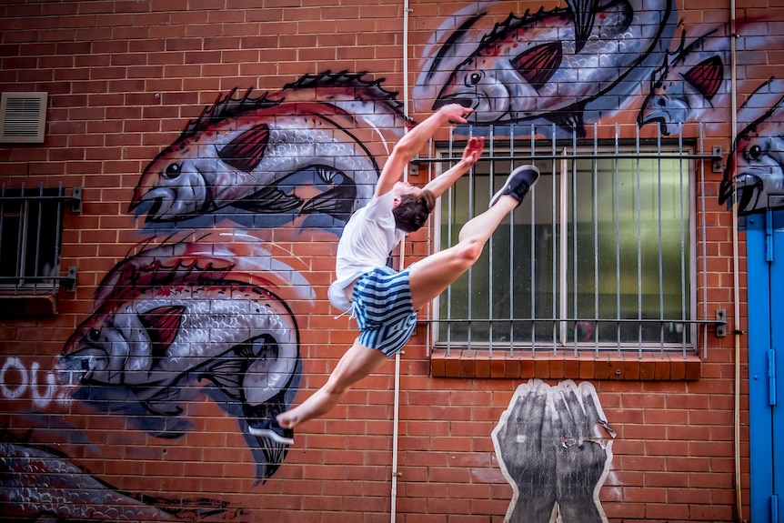 A young male ballet dancer jumps in the air in front of graffiti