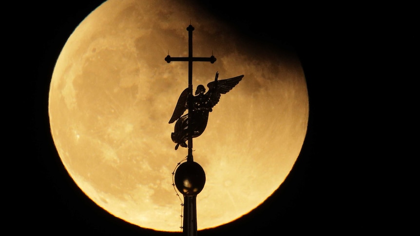 The city landmark weather vane in the form of an Angel is is silhouetted against the moon.