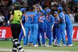 Indian cricket players celebrate with their hands raised as an Australian walks off in the foreground.