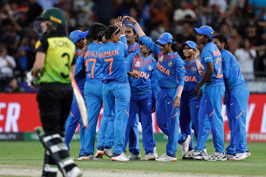 Indian cricket players celebrate with their hands raised as an Australian walks off in the foreground.