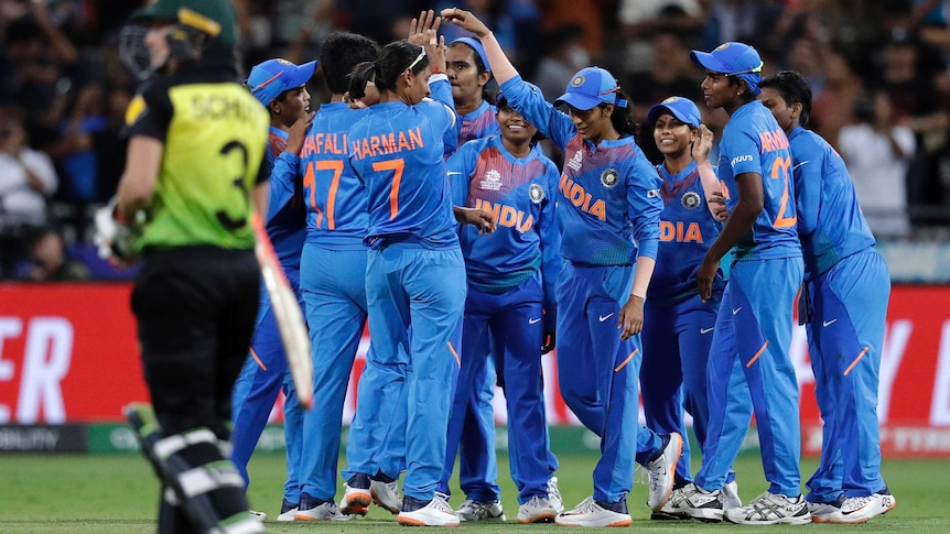 Indian cricket players celebrate with their hands raised as an Australian walks off in the foreground.