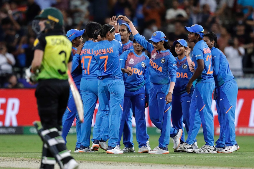 Indian cricket players celebrate with their hands raised as an Australian walks off in the foreground.