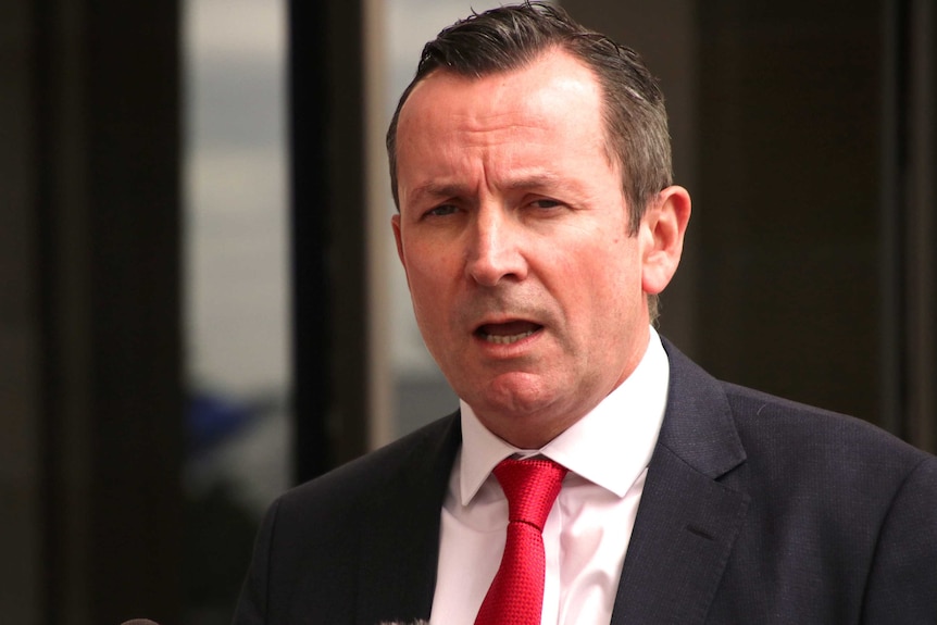 A tight head and shoulders shot of WA Premier Mark McGowan speaking wearing a black suit, white shirt and red tie.