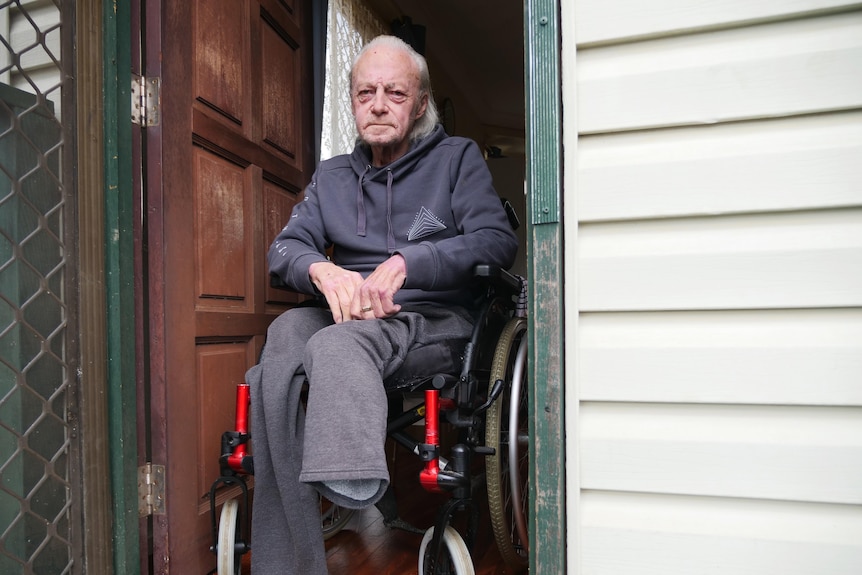 Човек без крака седи в инвалидна количка на вратата си