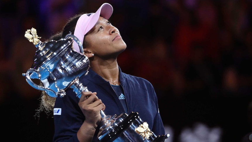 Naomi Osaka holds the winner's trophy and looks to the sky with a smile.