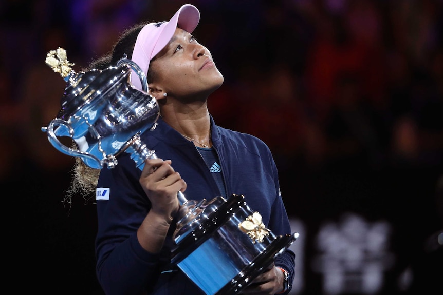 Naomi Osaka holds the winner's trophy and looks to the sky with a smile.