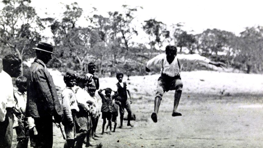 A boy jumps in the air as a crowd of other boys looks on.