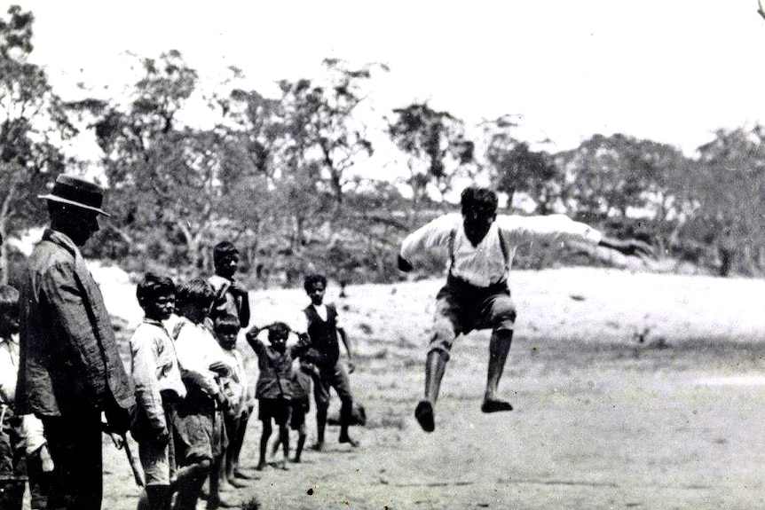 A boy jumps in the air as a crowd of other boys looks on.