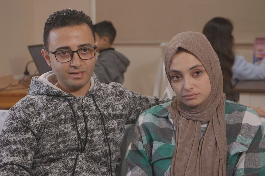Rami is sitting with his wife Yasmine (right) who is wearing a green and balck checkered shirt. Two of their children are shown
