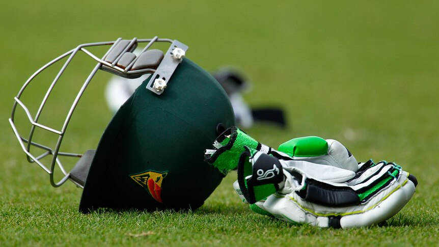 A Tasmanian Tigers player's cricket helmet and gloves sit on the grass.