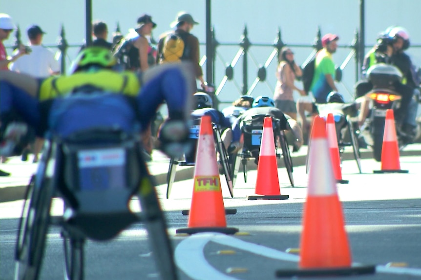 Wheelchair races compete along a road lined with traffic cones.
