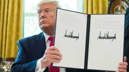 President Donald Trump holds up a signed executive order as two men stand either side of his desk.