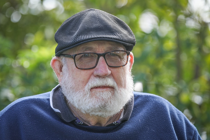 An elderly man with a white beard looks stern.