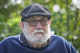 An elderly man with a white beard looks stern.