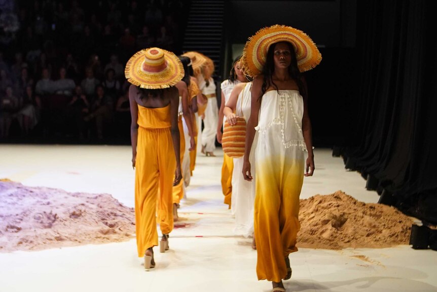 a fashion runway with seven models wearing white and yellow dresses.