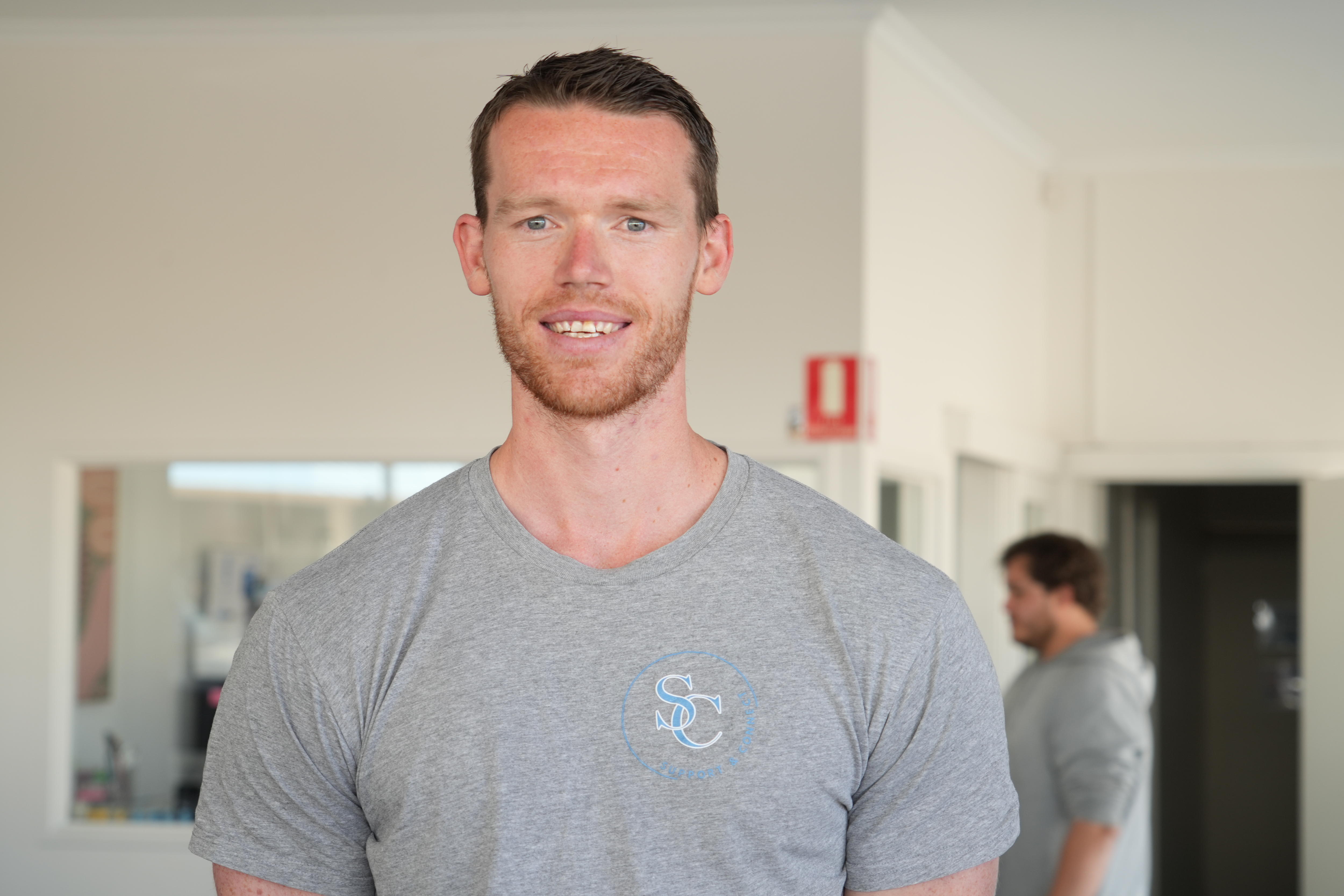 A close up portrait of a young man in a grey t-shirt smiling.
