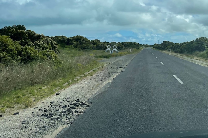 Bit of bitumen are strewn across the bush next to a highway.