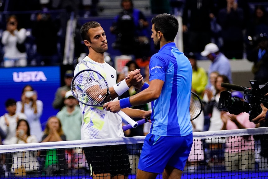 Two tennis players shake hands over a net. 