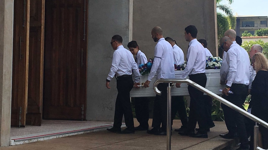 Men in white shirts carry a small white coffin up church steps.