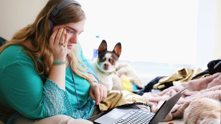 Young woman with autism and other learning disabilities using laptop for remote learning. A cute dog sits at her side.