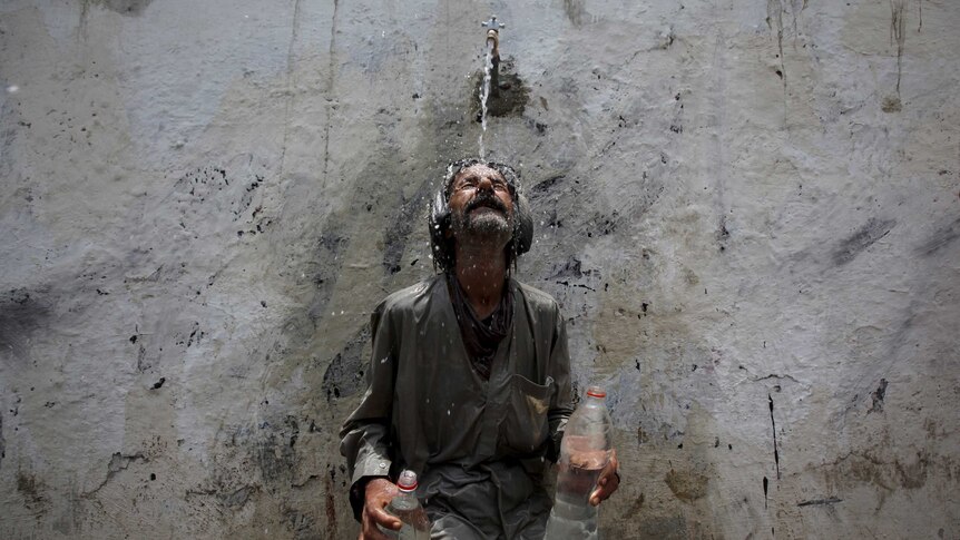 A man cools off from a public tap after filling bottles during intense hot weather in Karachi, Pakistan