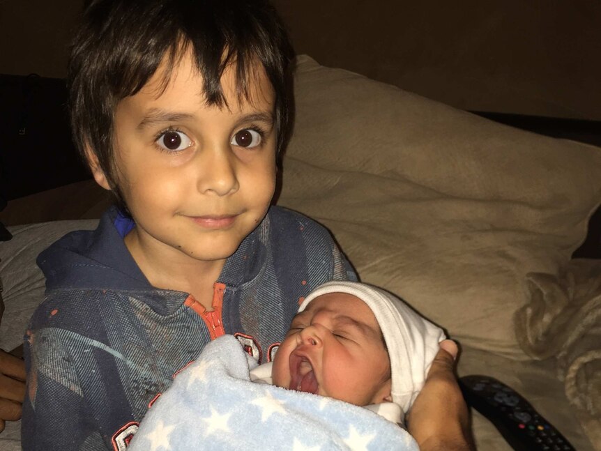 A photo of Kye Ryan smiling as he holds his newborn brother Raiden.