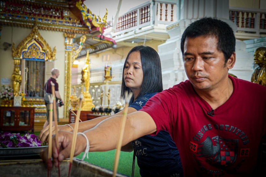 Thai man and woman putting incense sticks onto an altar at a temple.