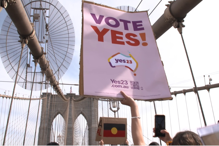 A Vote yes sign being held up with the Brooklyn Bridge in the background
