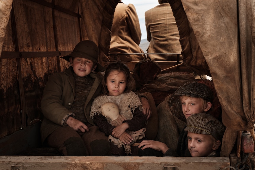 Four children dressed in 19th century gear, sitting together