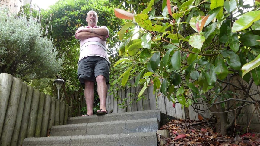 A man stands at the top of some outdoor concrete stairs and crosses his arms