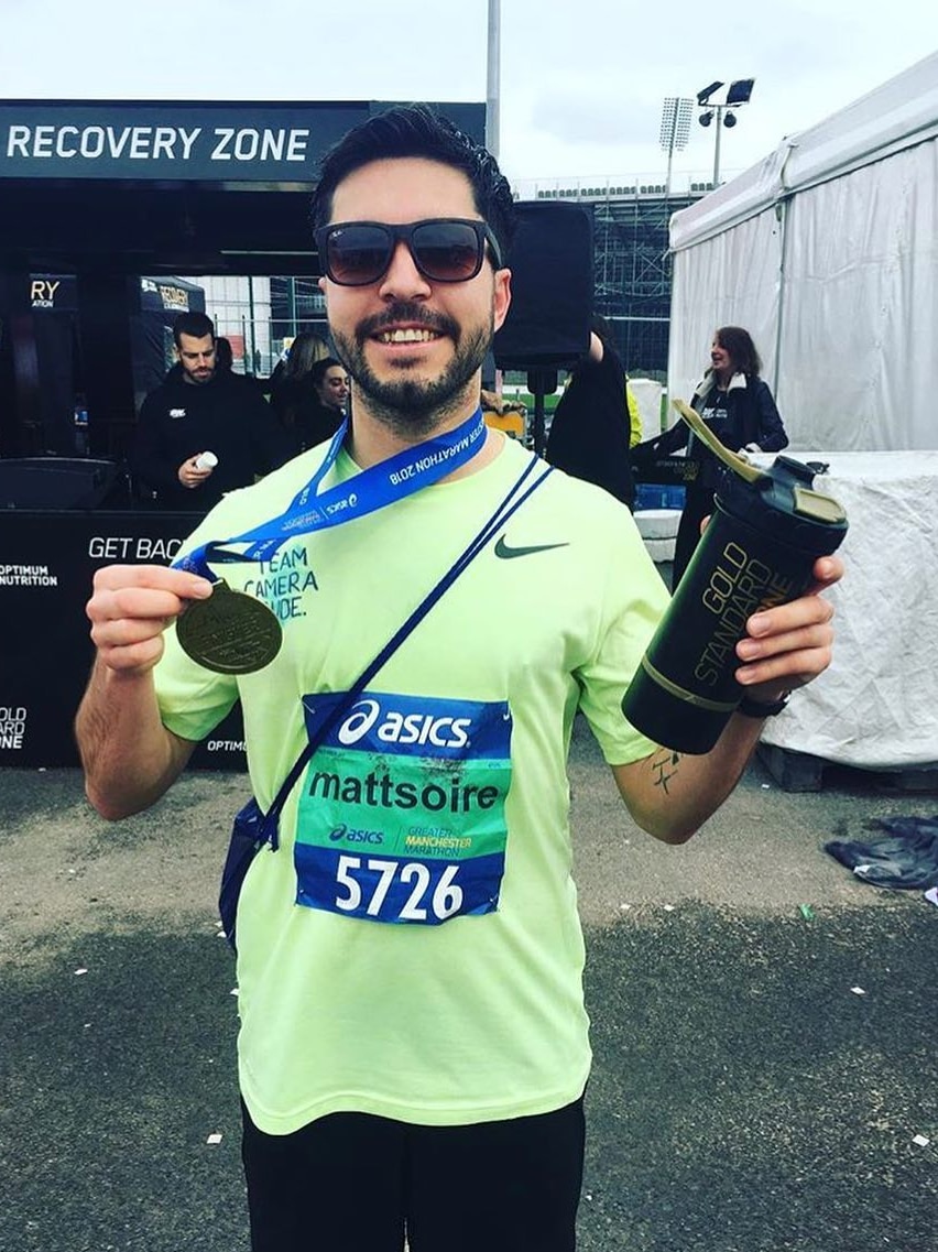 A man holds a medal and water bottle after completing the Manchester Marathon.