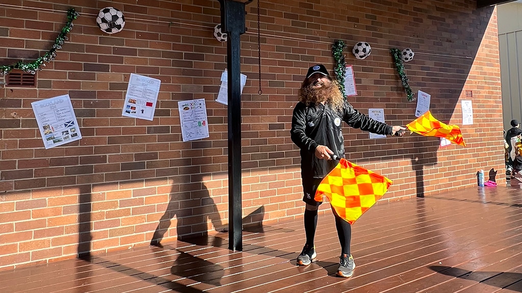 Costa wearing gym wear holding two orange and yellow chequered flags.