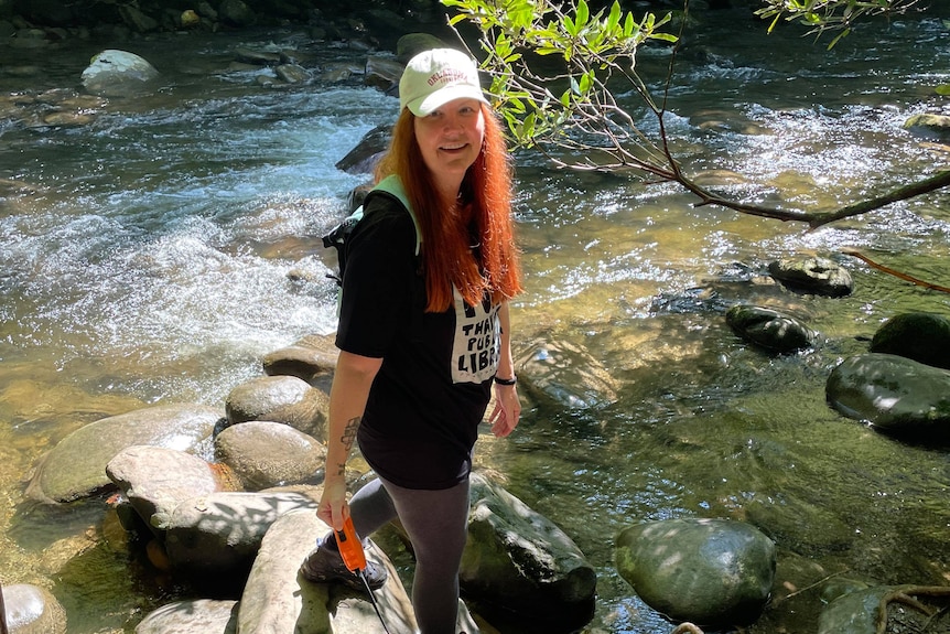 Shellie Zeigler with long red hair standing net to a flowing creek