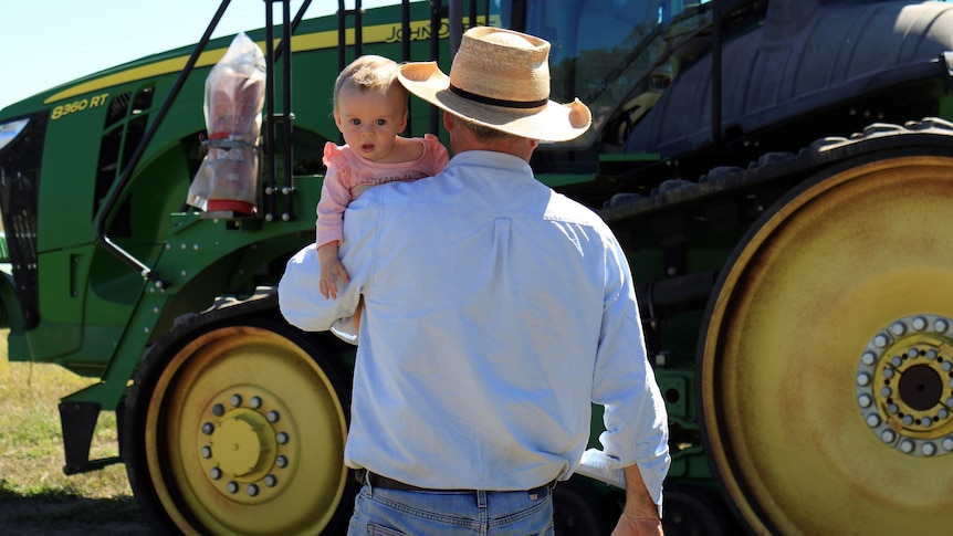 Burly farmer carries baby towards tractor